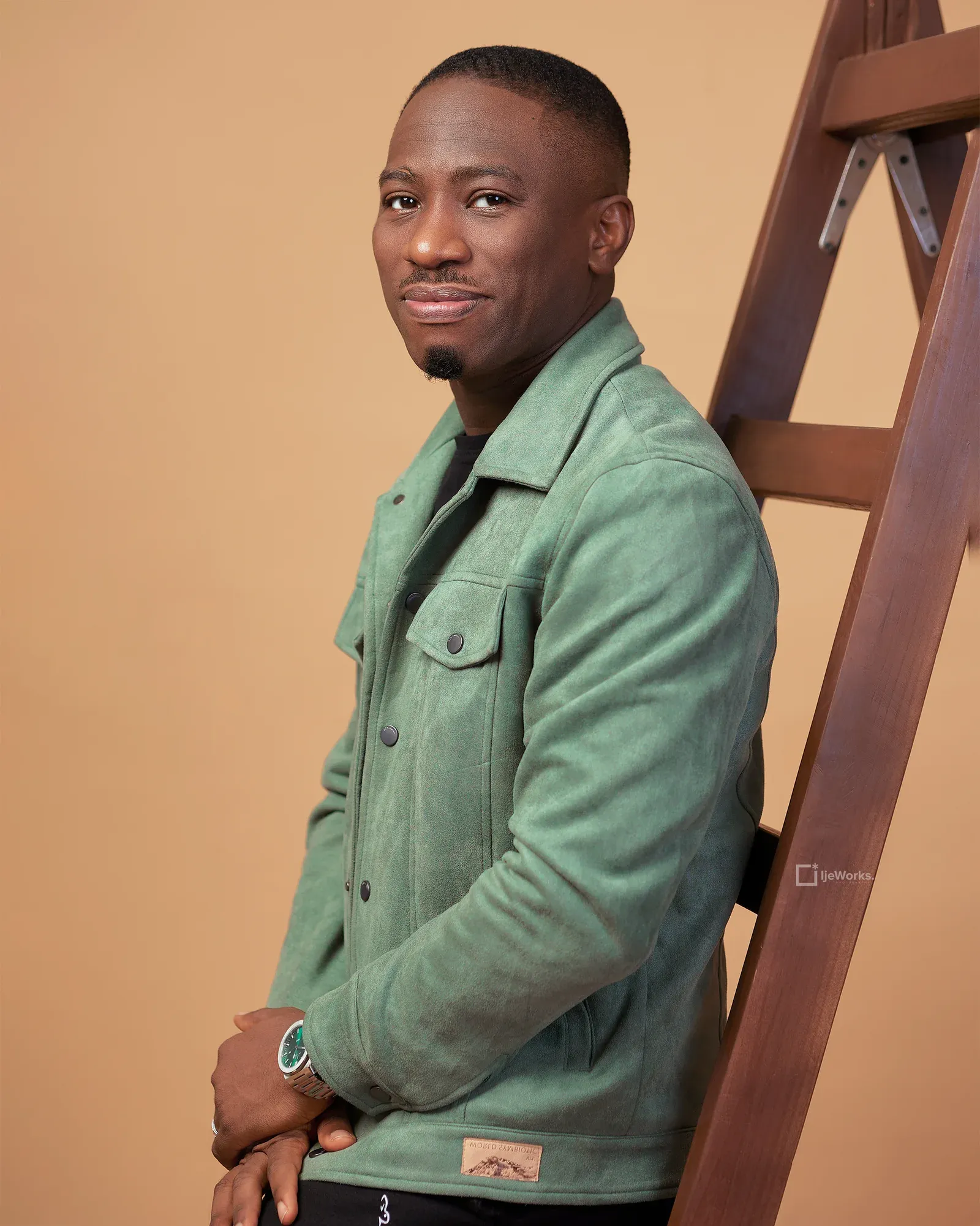 David Nkennor leaning against a wooden ladder in a green jacket.